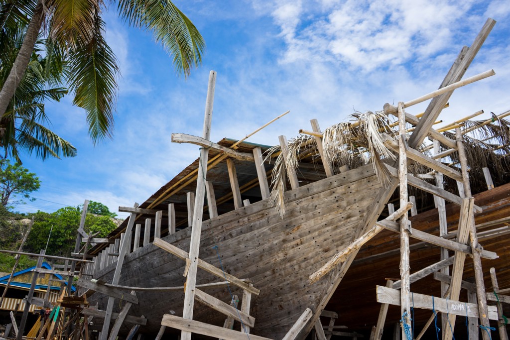 Traditionele houten boot in aanbouw op Sulawesi, Indonesië, onder palmbomen.
