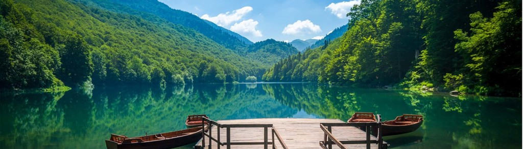 Houten steiger met bootjes aan een groen bergmeer tijdens een familiereis door Kroatië en Montenegro.