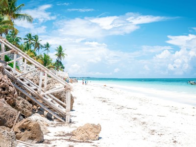 Wit zandstrand met palmbomen en houten trap langs de rotsen aan de kust van Tanzania.