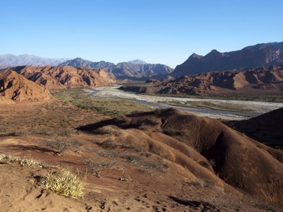 Rode rotsformaties en een rivierdal in het Andesgebergte tijdens de Route Argentinië.