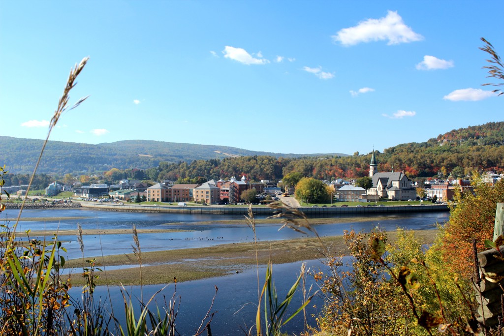 Rivierlandschap in Oost-Canada met dorp, kerk en herfstkleuren in de heuvels onder een blauwe lucht.