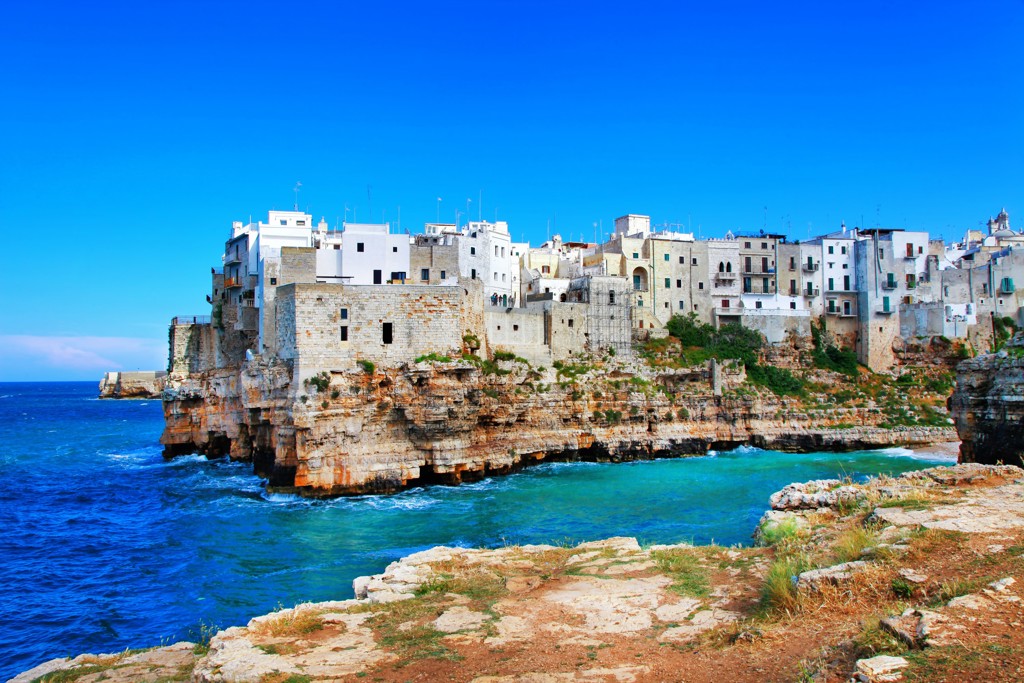 Witte huizen op kliffen aan de Adriatische kust in Puglia, Italië, met helderblauwe zee en lucht.