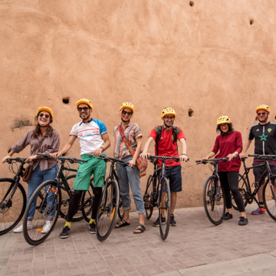 Groep fietsers met helmen poseert met fietsen voor een lemen muur tijdens een fietsvakantie in Marokko.