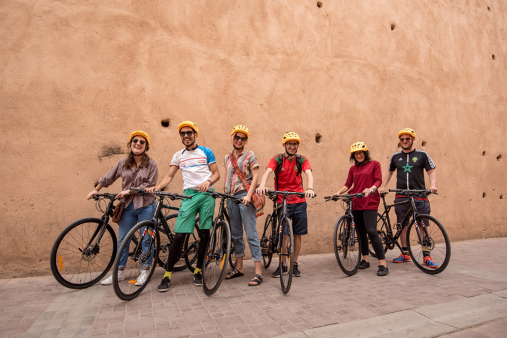 Groep fietsers met helmen poseert met fietsen voor een lemen muur tijdens een fietsvakantie in Marokko.