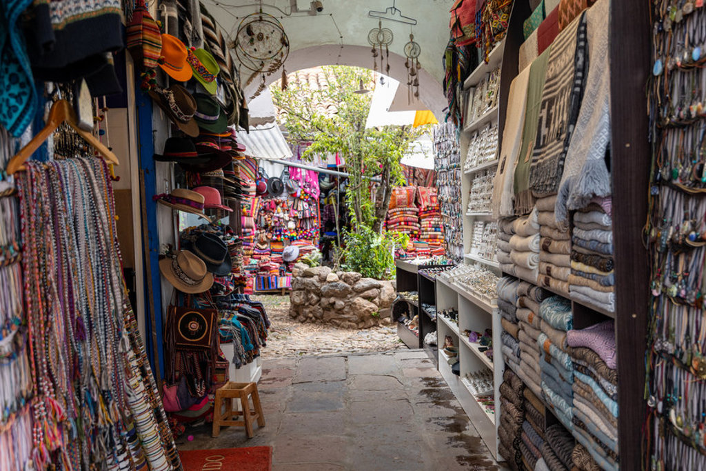Marktstraatje in Peru met kleurrijke textiel, hoeden en souvenirs tijdens een 22-35ers groepsrondreis.