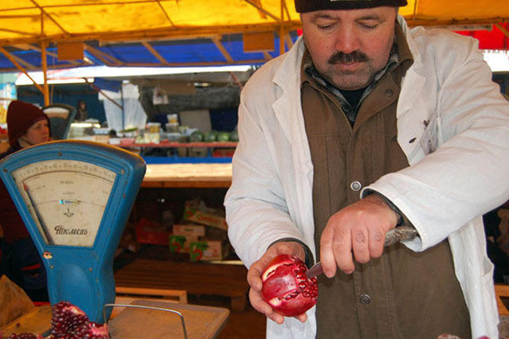 Marktverkoper op een Russische wintermarkt snijdt een granaatappel open.