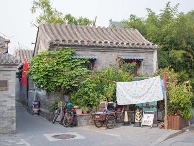 Traditionele hutongwoning in China met grijze dakpannen, fietsen en hangend wasgoed in een groene binnenplaats.