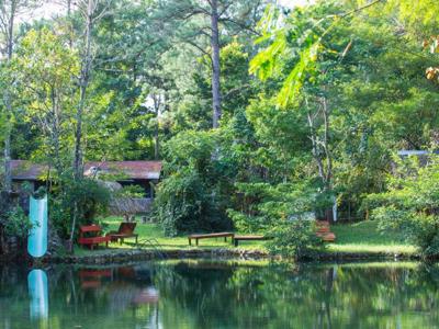 Lodge aan een rustig meer in het groene regenwoud van Guatemala, met ligbedden en kano aan de oever.