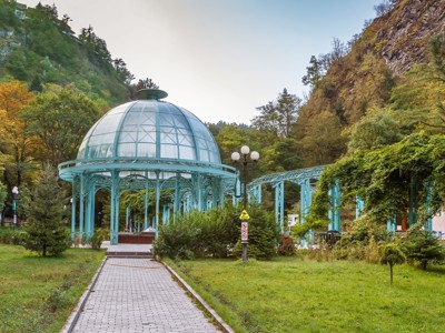 Glazen koepelpaviljoen in het Borjomi-park, Georgië, omringd door groen en bergen.