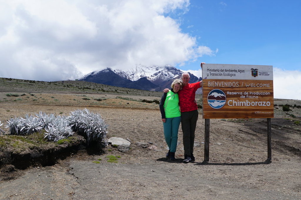 Reizigers bij het welkomsbord van Reserva de Producción de Fauna Chimborazo in Ecuador, met de besneeuwde vulkaan op de achtergrond.