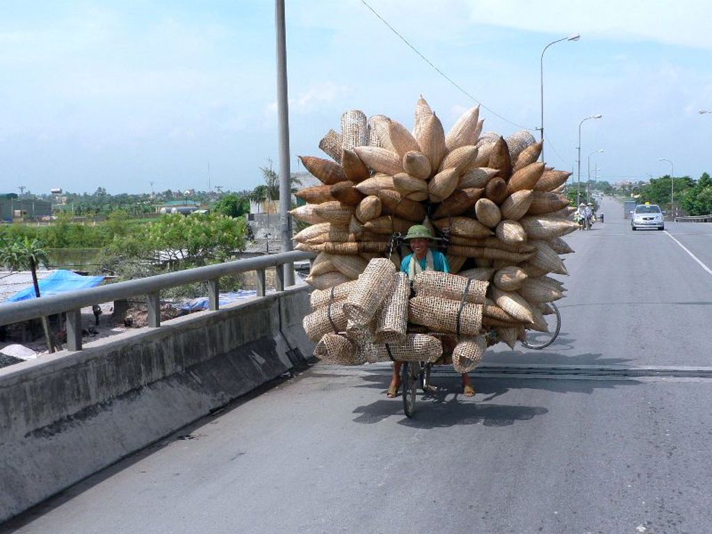 Fietser in Vietnam vervoert een enorme lading rieten manden over een brug.