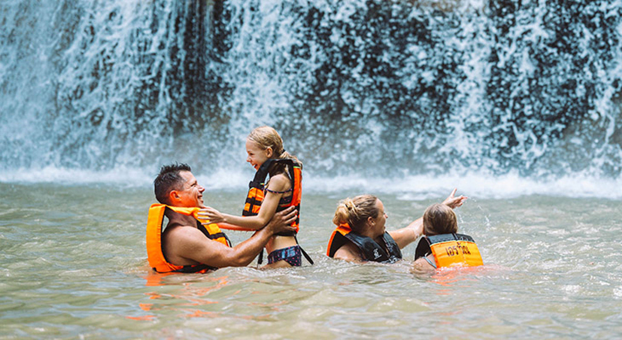 Gezin met zwemvesten zwemt en speelt in het water bij een waterval.