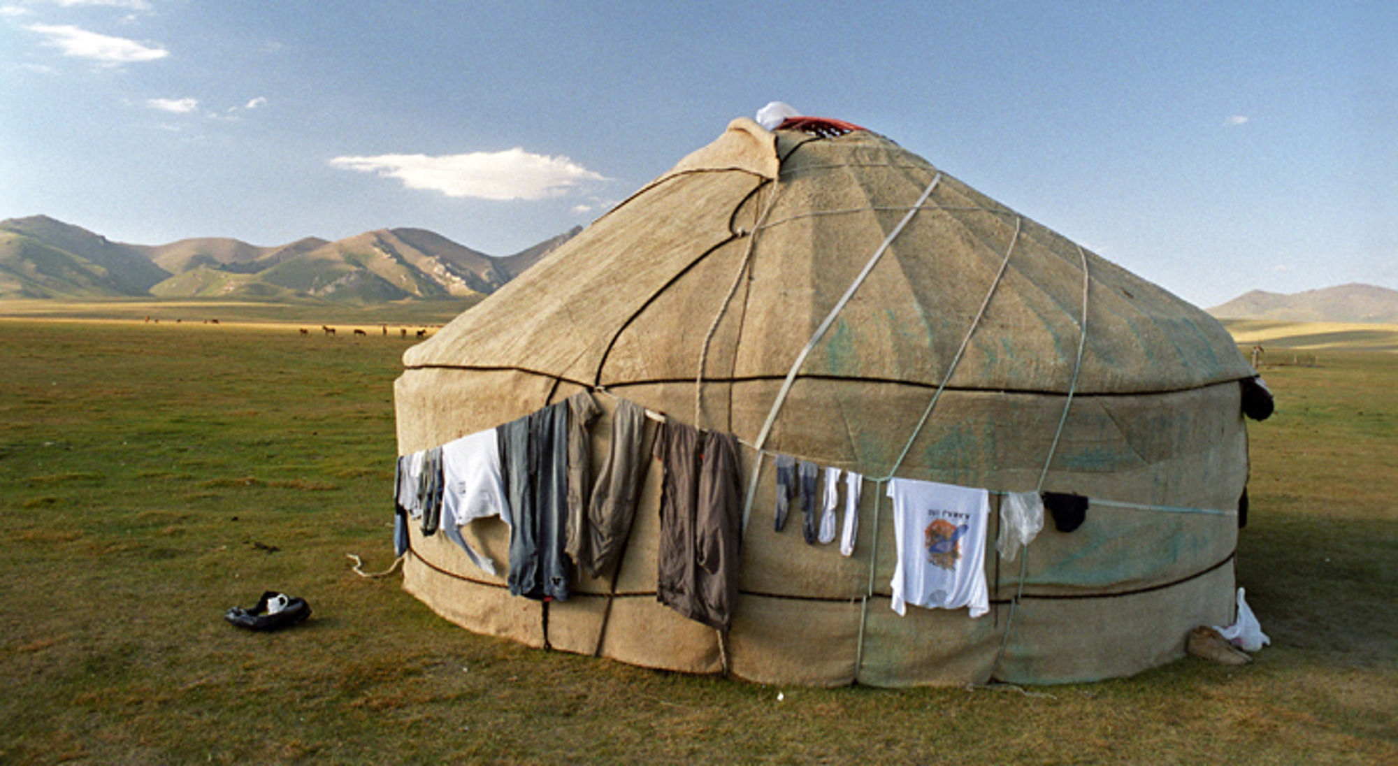 Ger langs de Zijderoute Ronde yurt op de Mongoolse steppe met bergen op de achtergrond en wasgoed aan de buitenkant.