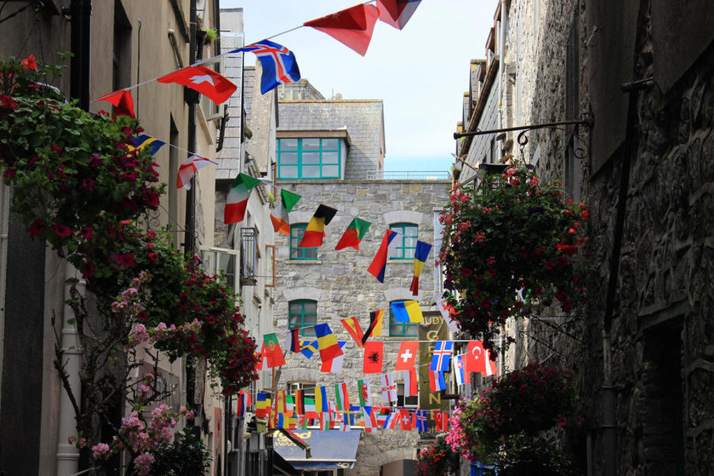 Smalle straat in Ierland met kleurrijke vlaggenlijnen en bloemen aan gevels.