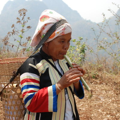Vrouw in traditionele kleding speelt bamboefluit in het berglandschap van Thailand tijdens een groepsrondreis.