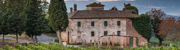 Toscaans landhuis tussen cipressen en wijngaarden, met heuvels op de achtergrond.