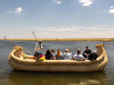 Groep reizigers vaart in een traditionele rieten boot over het Titicacameer in Peru.