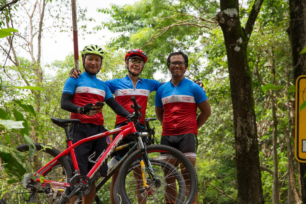 Drie fietsers poseren met mountainbike in groene natuur tijdens fietsvakantie Vietnam, Cambodja en Thailand.
