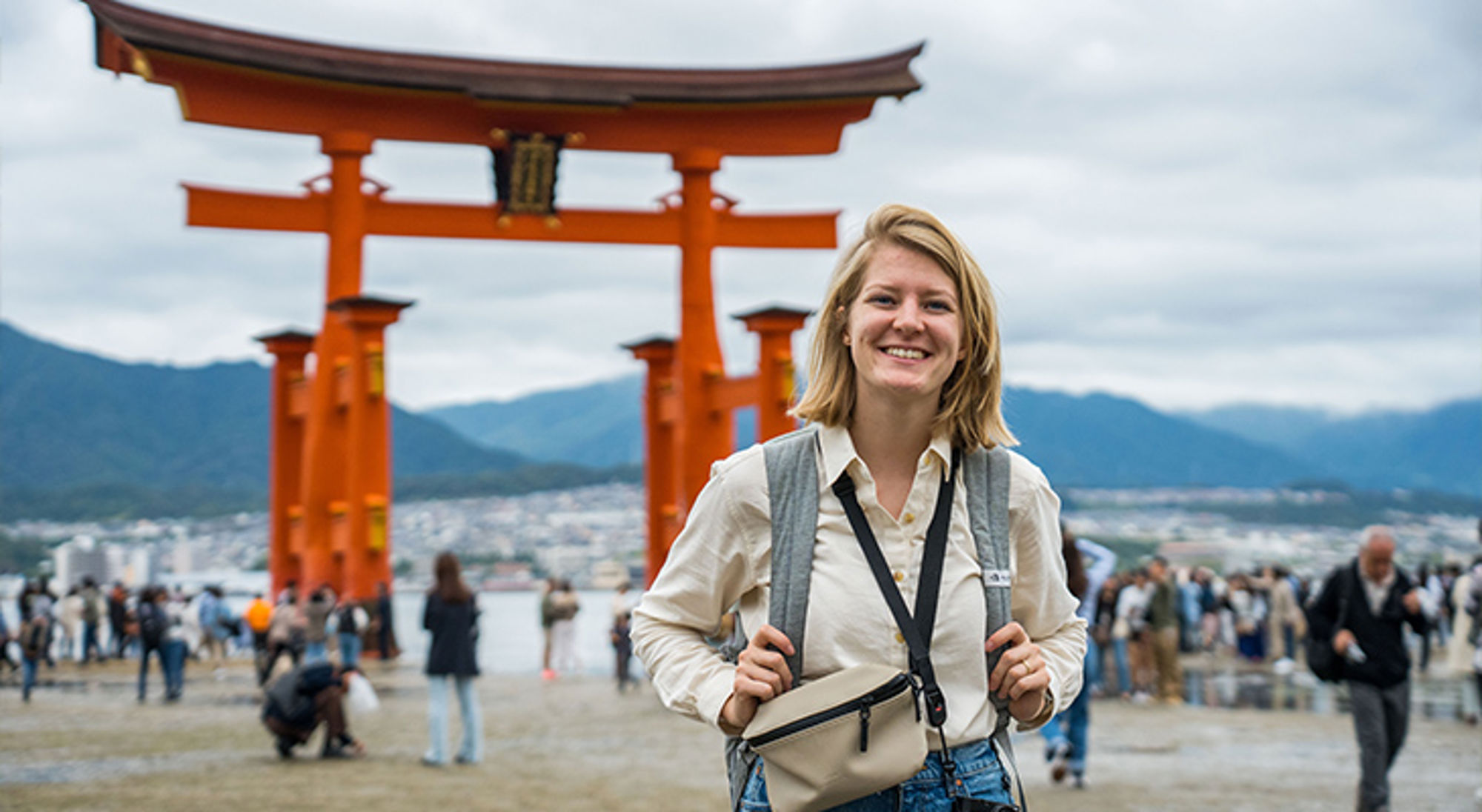 Reiziger poseert bij de rode torii-poort van Itsukushima-schrijn op Miyajima, Japan.
