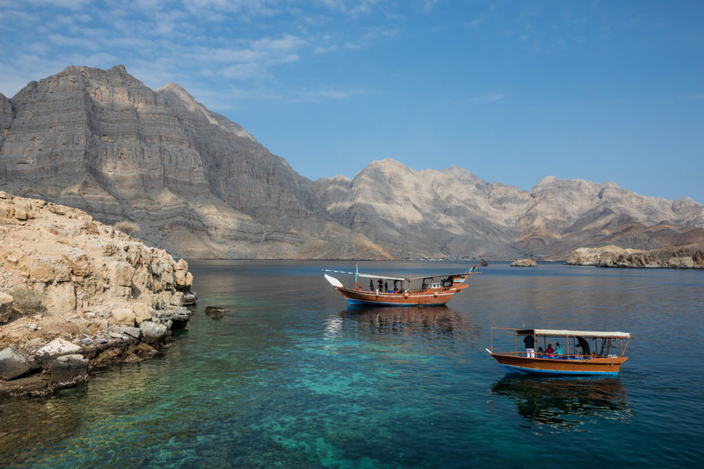 Dhowboten op helderblauw water bij de rotsachtige kust en bergen van Oman tijdens groepsrondreis Oman en Dubai.