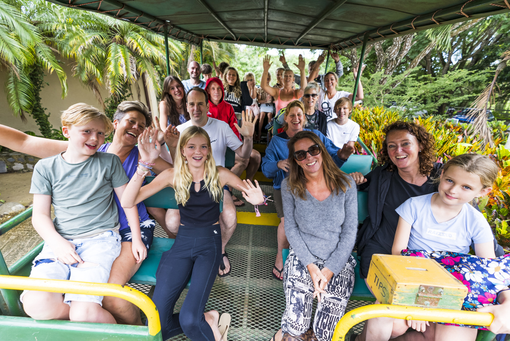 Gezinnen tijdens familiereis Costa Rica zwaaien vanuit een open safariwagen in het groen.