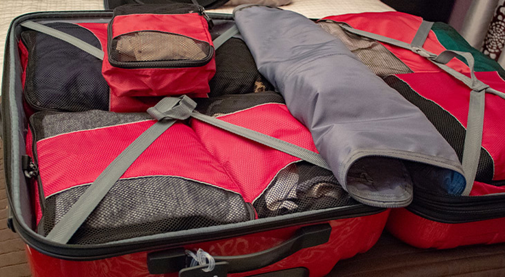 Cadeau voor reiziger packing cubes Open reiskoffer met rode packing cubes en opgerolde kleding, klaar voor vertrek.