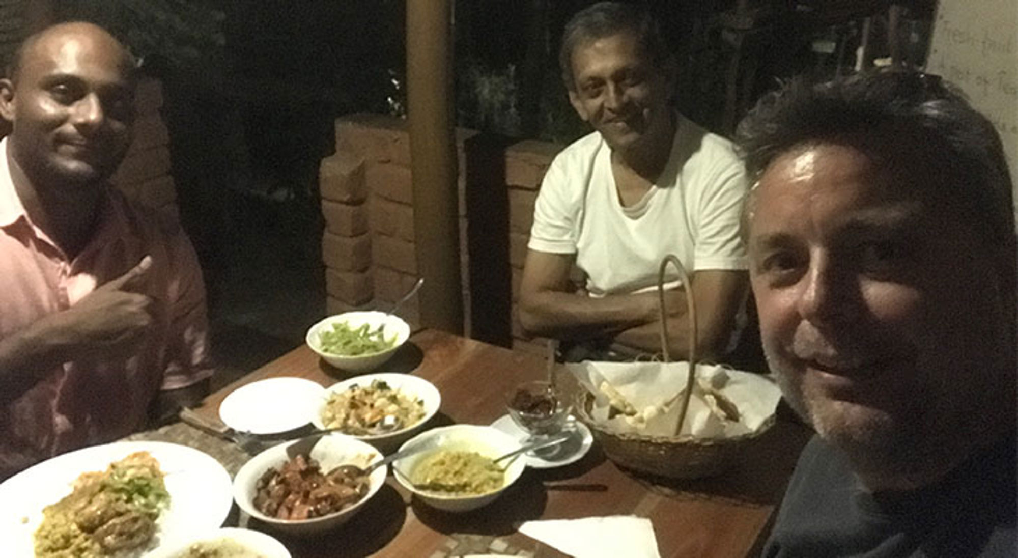 Drie mannen aan tafel met lokale gerechten en broodmand tijdens een avondmaaltijd.