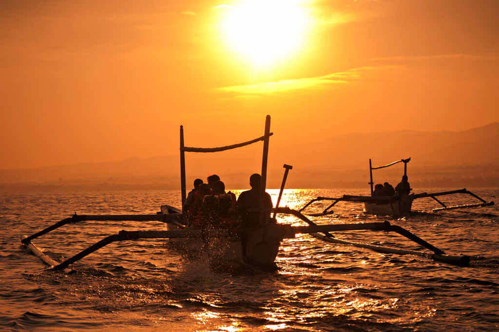 Traditionele boot met reizigers bij zonsondergang op zee tijdens familiereis Java en Bali.