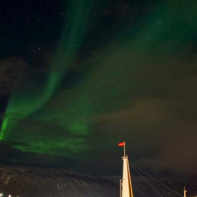 Groen noorderlicht boven de mast van zeilschip Antigua tijdens een groepsrondreis in Noorwegen.