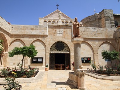 Binnenplaats van de Sint-Catharinakerk in Bethlehem met standbeeld en stenen gevel.