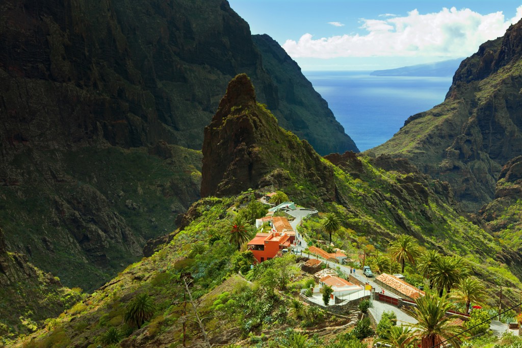 Uitzicht op bergdorp in de Masca-kloof op Tenerife, met palmen en de Atlantische Oceaan op de achtergrond.