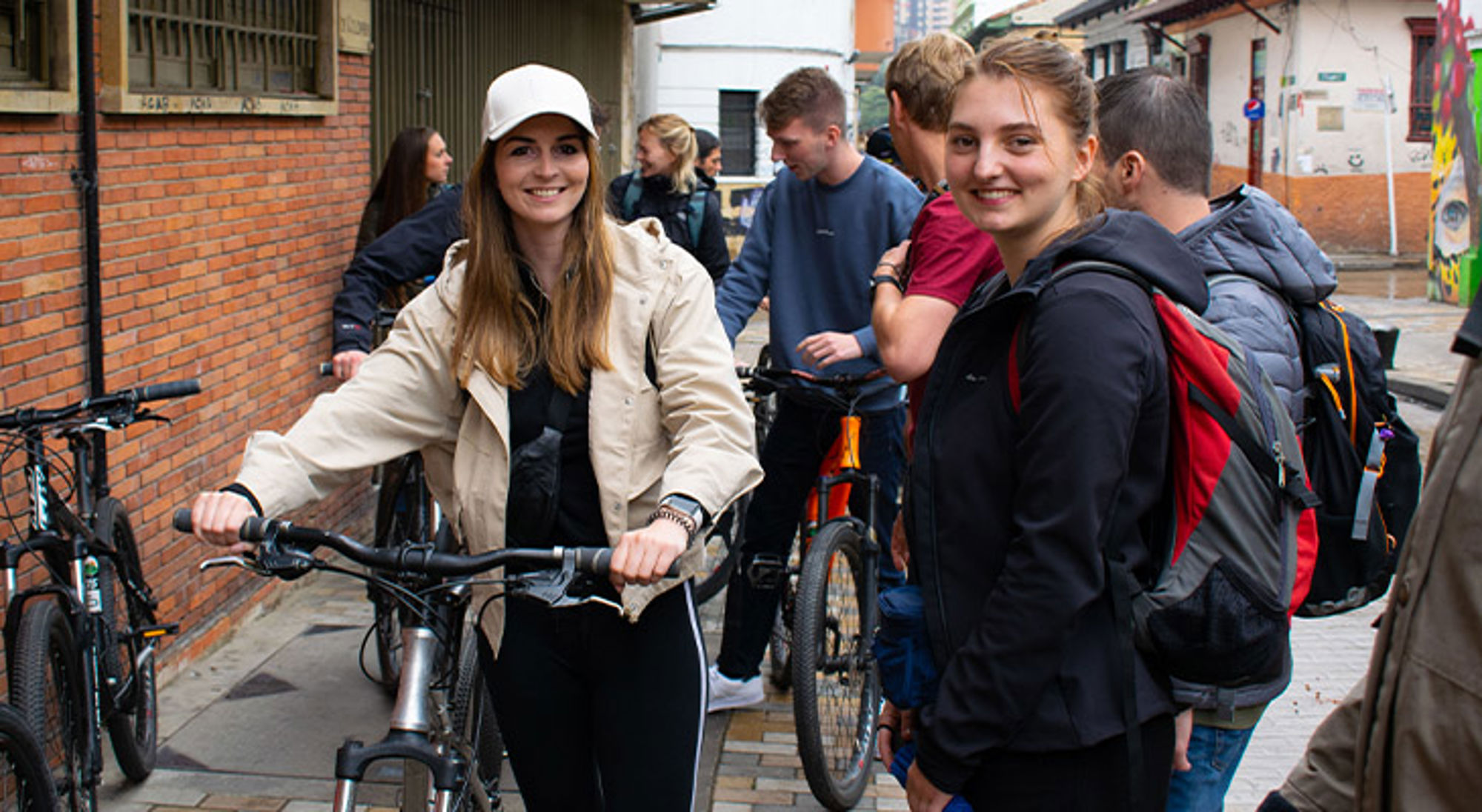 Fietsen in Bogota Groep jongeren met rugzakken en fietsen in een straat, met twee lachende vrouwen op de voorgrond.