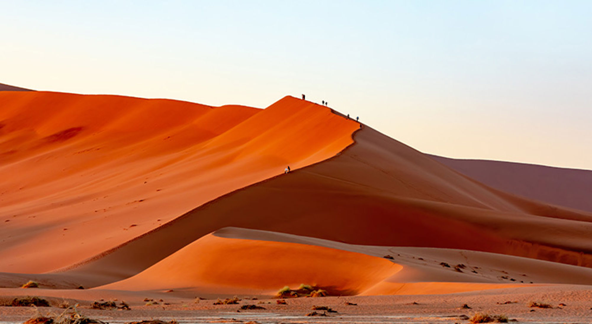 Sossusvlei Oranje zandduinen in de woestijn bij zonsondergang, met wandelaars op de kam.