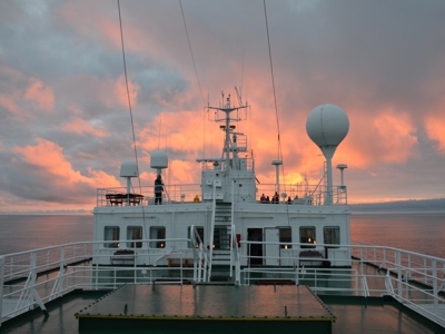 Dek van expeditiecruiseschip tijdens route vier Arctische eilanden, met zonsondergang boven zee.