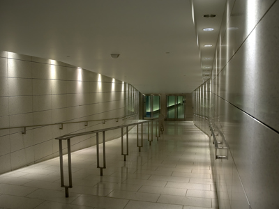 Ondergrondse gang met metalen leuningen en verlichting, richting de uitgang.