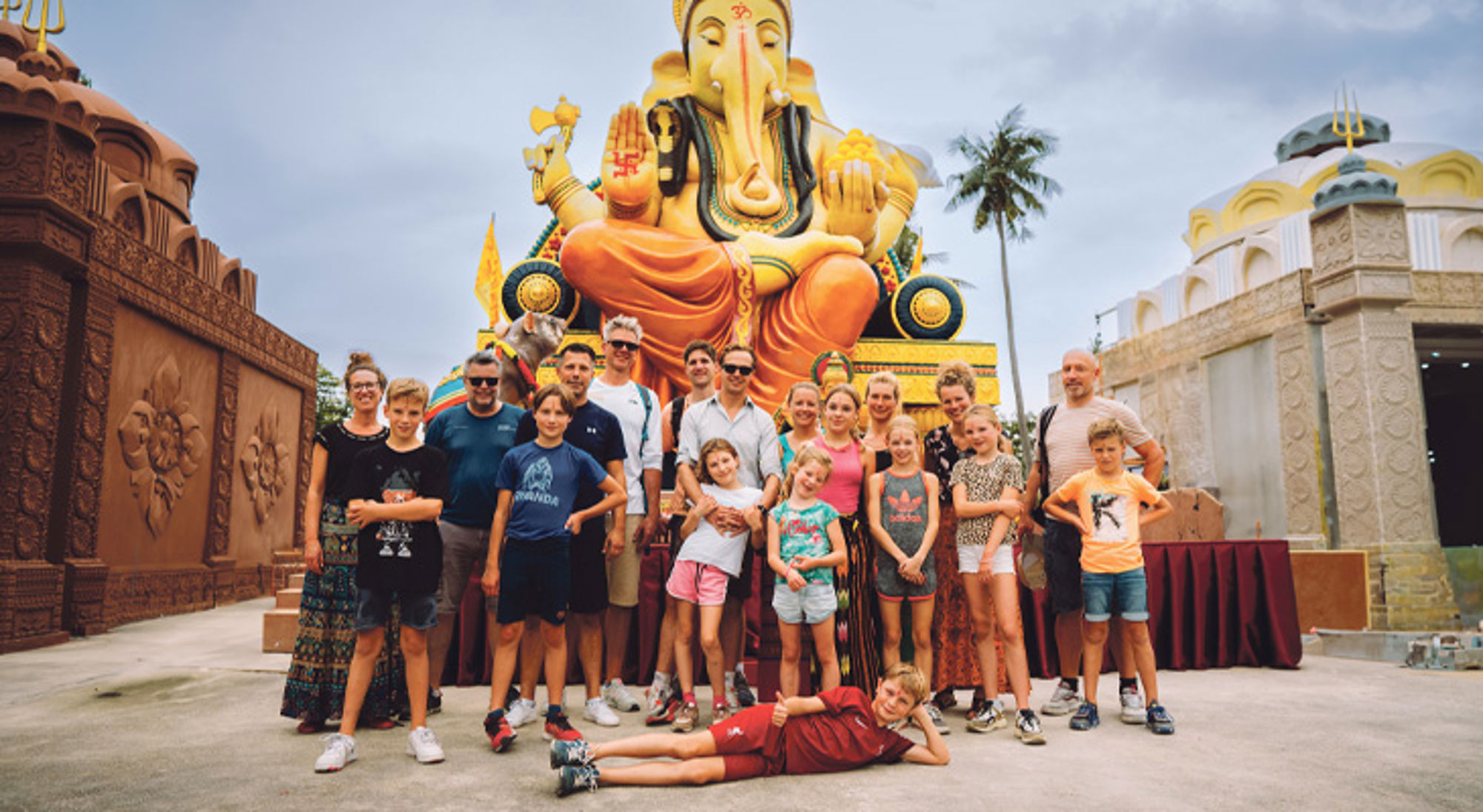 Families Thailand Groepsfoto van reizigers voor een groot Ganesha-beeld bij een tempelcomplex.