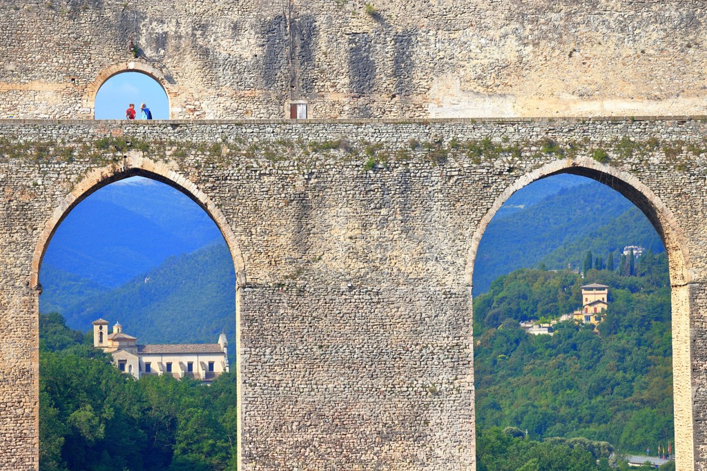 Wandelaars op een stenen aquaduct met uitzicht op groene heuvels in de Centrale Apennijnen, Italië.