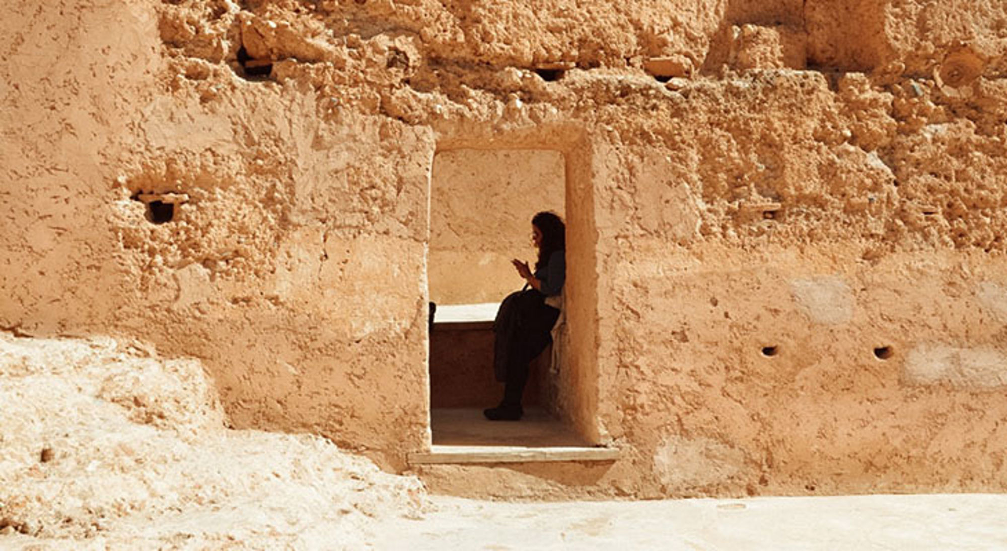 EL-Badi paleis Vrouw zit in een nis van een lemen muur en kijkt op haar telefoon.