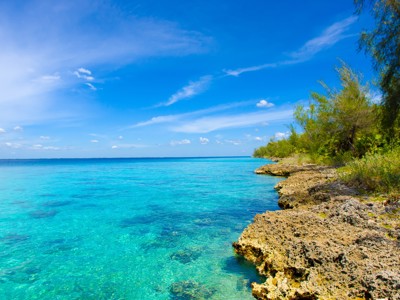 Rotsachtige kust met helderblauw zeewater en groene begroeiing langs de oever in Cuba.
