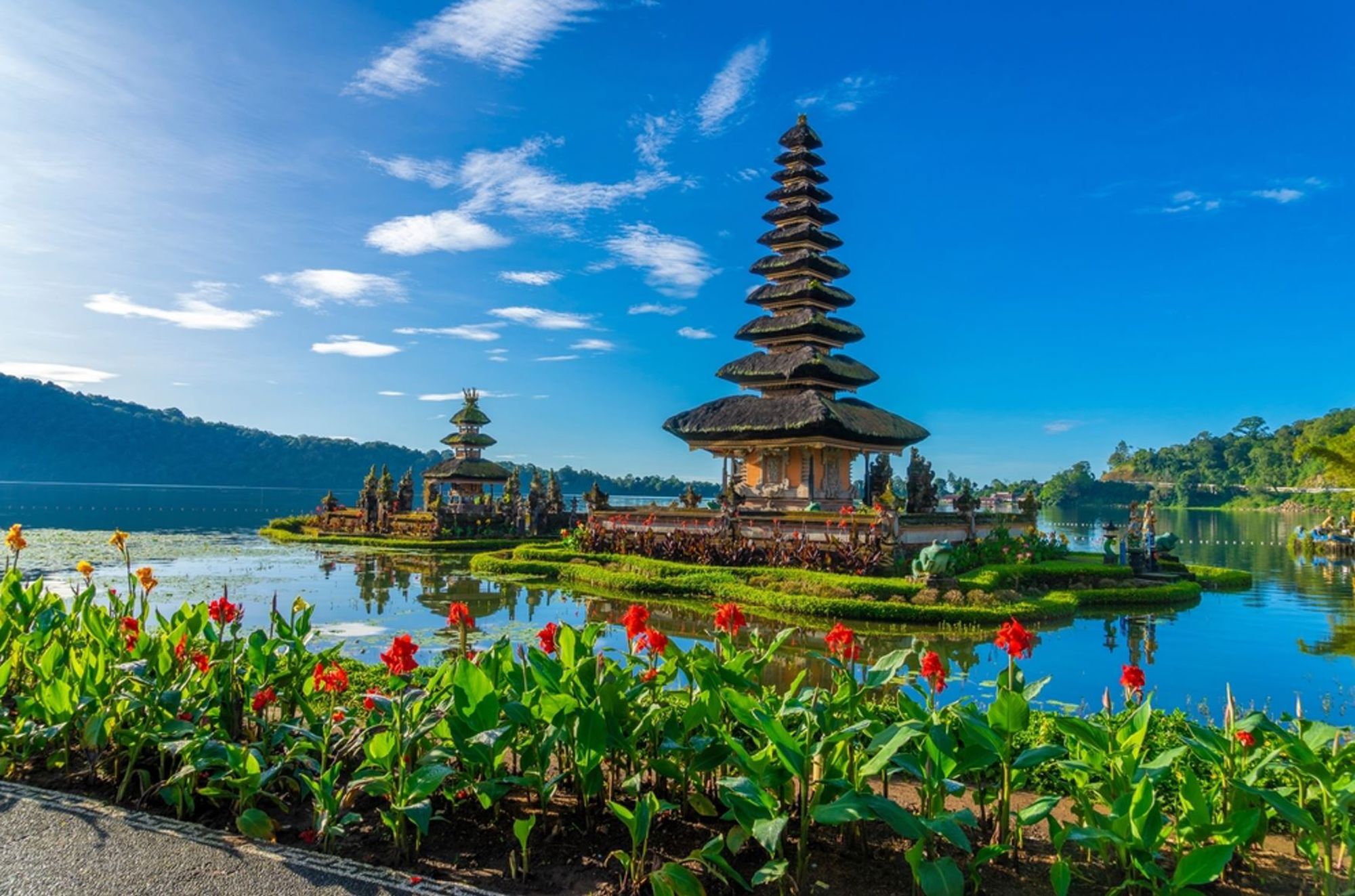 Pura Ulun Danu Bratan-tempel aan het Bratanmeer op Bali, met bloemen op de voorgrond en blauwe lucht.