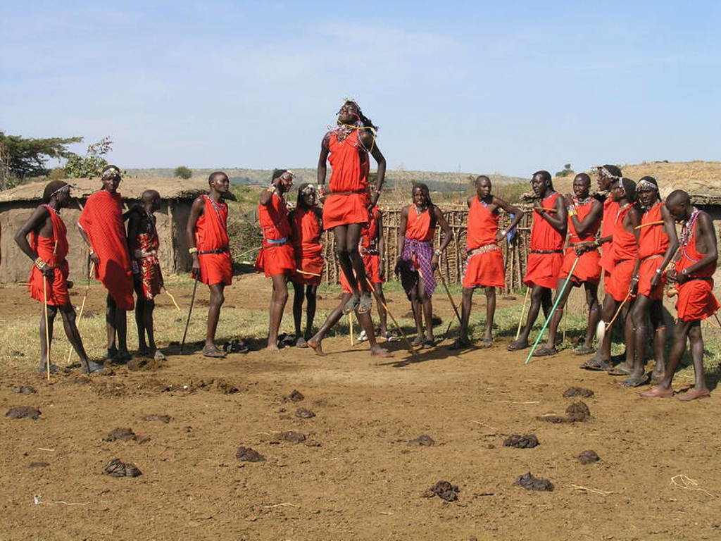 Traditionele dans met springende Maasai-krijger en groep in rode kledij tijdens groepsrondreis Kenia en Tanzania.