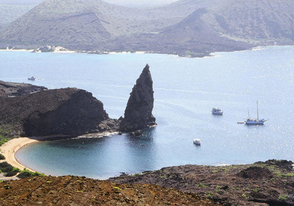 Vulkanische kust met rotsformatie en boten in een baai op de Galapagoseilanden tijdens een groepsrondreis.