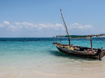 Traditionele dhowboot aan het strand van Zanzibar, met helderblauwe zee en witte zandkust.
