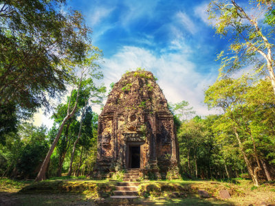 Oude tempelruïne in het bos langs de Route Indochina, met stenen trap en blauwe lucht.