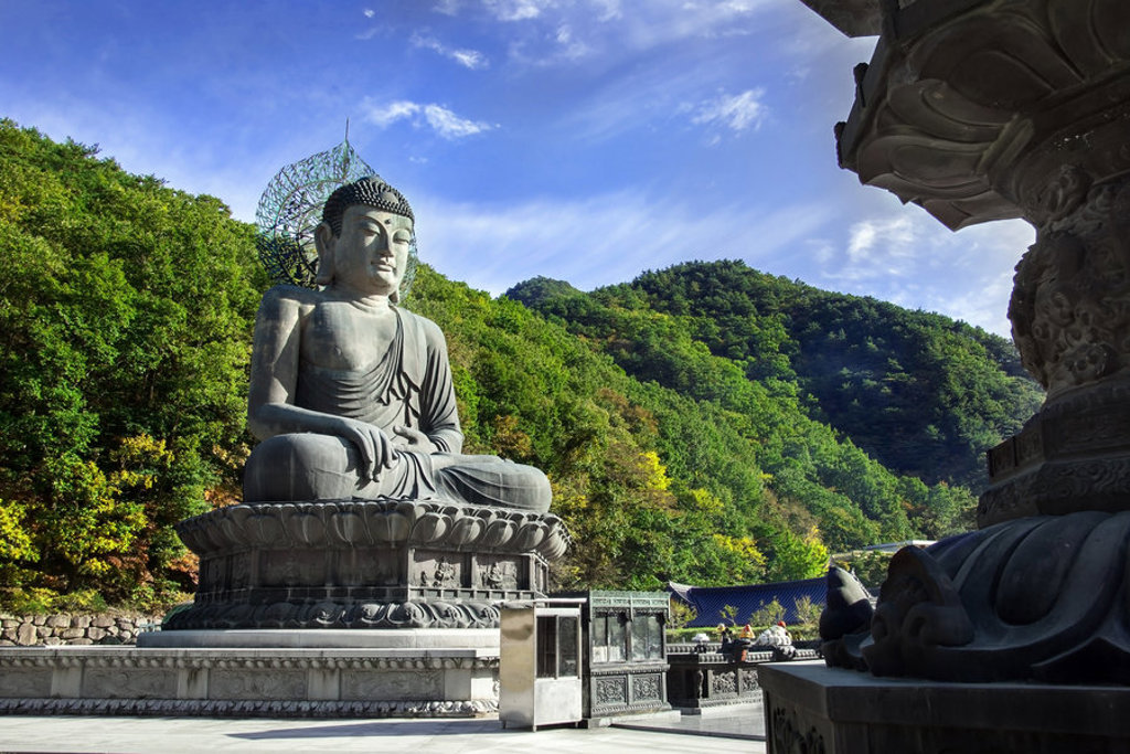 Grote Boeddhabeeld bij tempel in Zuid-Korea, omringd door groene bergen onder een blauwe lucht.