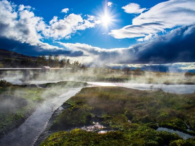 Stoom stijgt op uit warmwaterbronnen in IJsland, met kronkelende beekjes onder een heldere zon.
