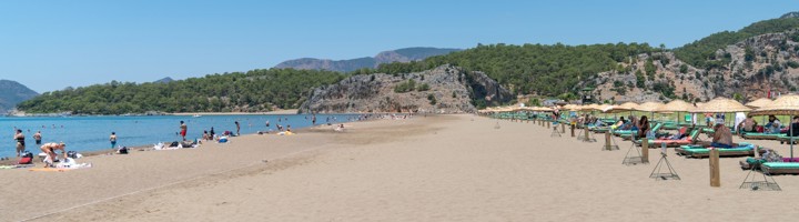 Breed zandstrand van Iztuzu Beach in Turkije met ligbedden, parasols en zwemmers langs helderblauw water.