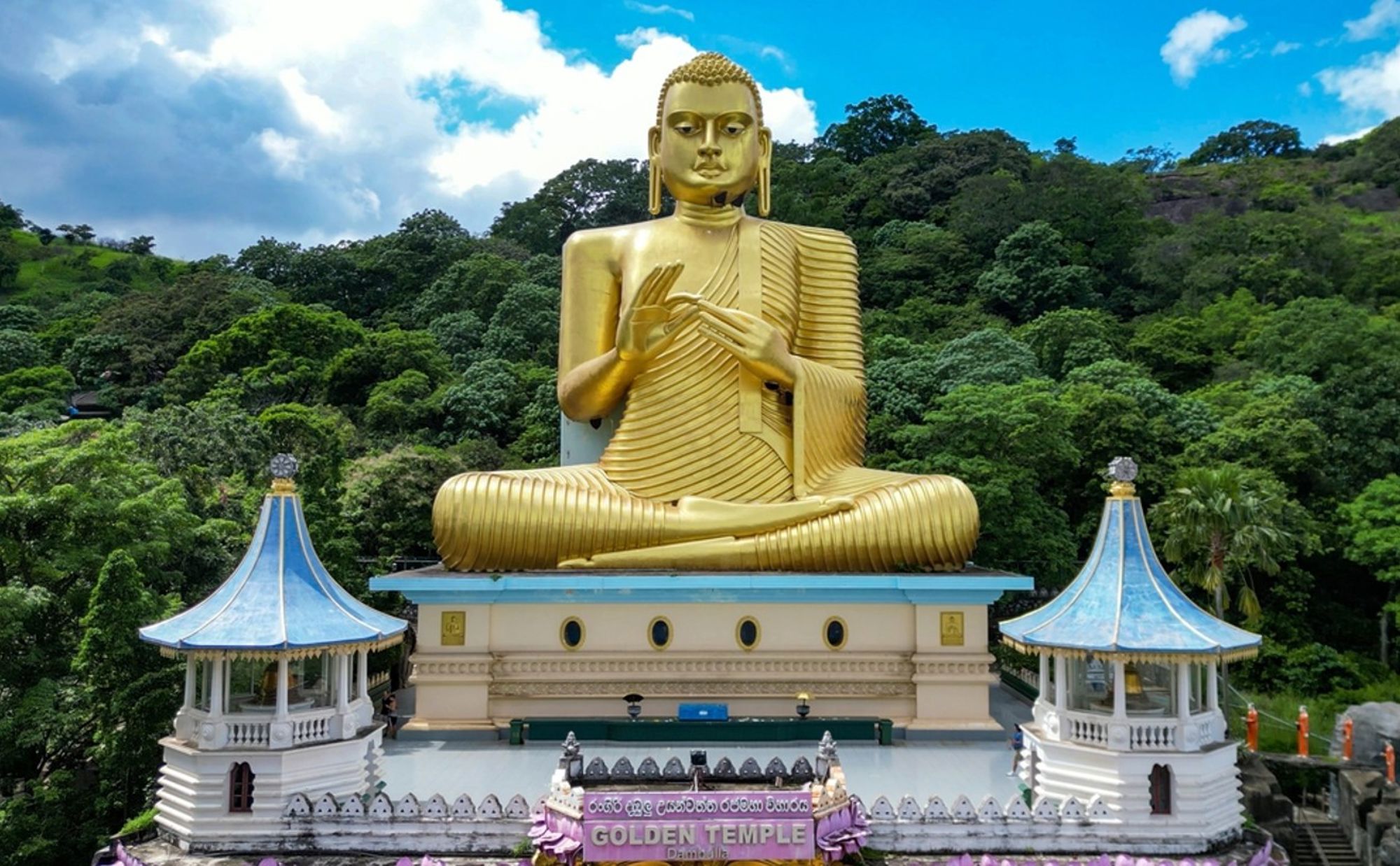 Gouden Boeddhabeeld bij Golden Temple in Dambulla, Sri Lanka, met groene heuvels op de achtergrond.