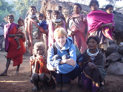 Reiziger poseert met dorpsbewoners bij rieten hutten tijdens Route Orissa, 23 dagen.