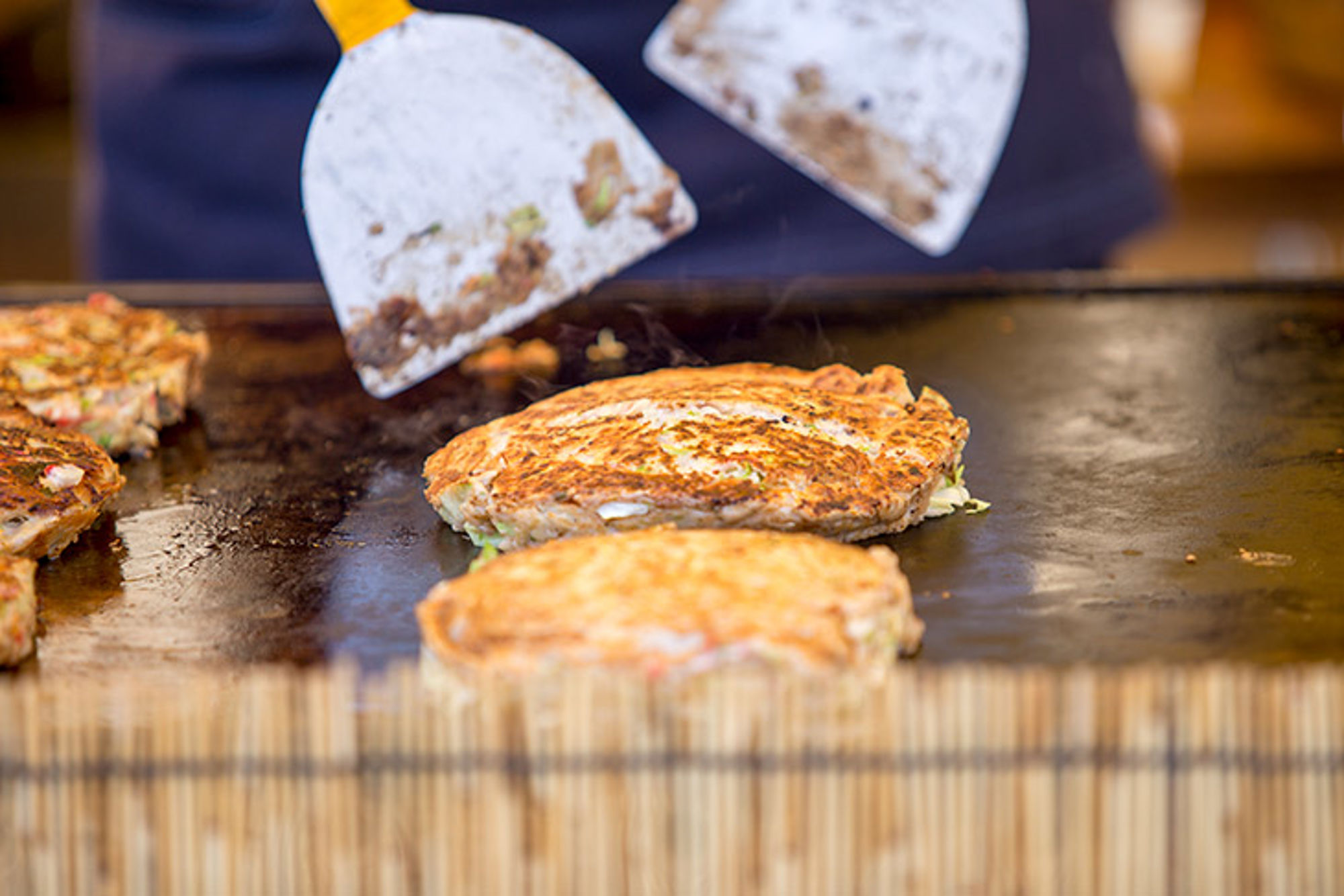 Okonomiyaki, Japan Okonomiyaki pannenkoeken op een bakplaat, bereid met spatels bij een teppanyaki-grill.